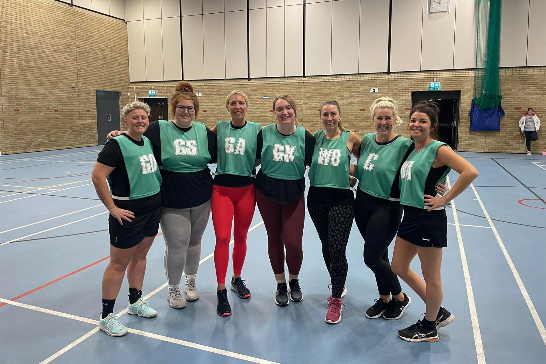 Image of a netball team in green bibs posing for a photo in a sports hall